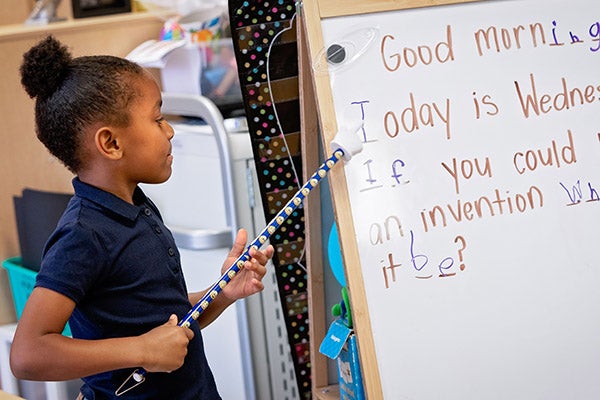 An ECU Community School student works on a problem at a white board.