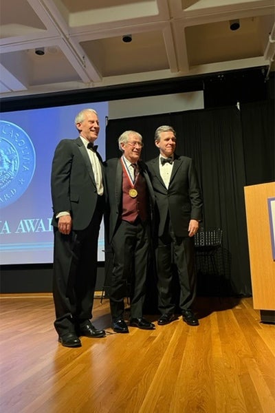East Carolina University professor emeritus and distinguished professor of geological sciences Stanley Riggs, center, is presented the North Carolina Award by North Carolina Secretary Reid Wilson and Governor Roy Cooper.