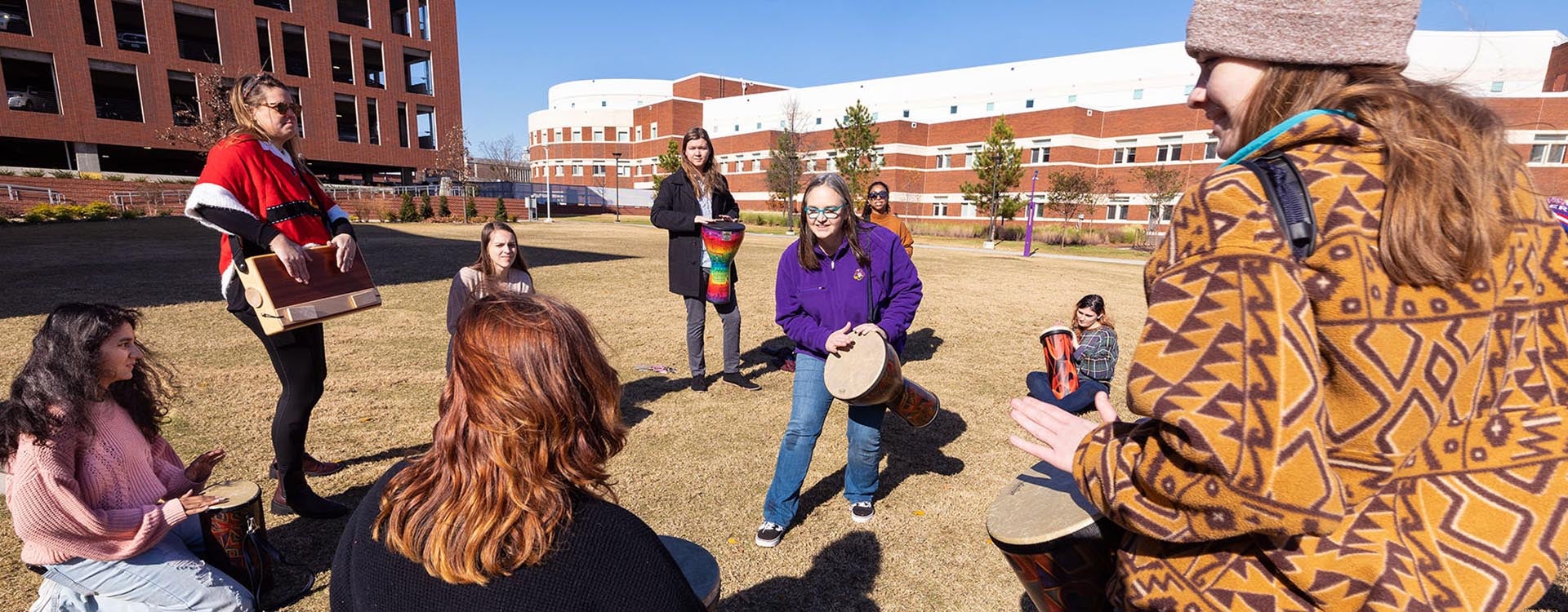 Assistant professor Virginia Driscoll leads students in group drumming outside at the student center.