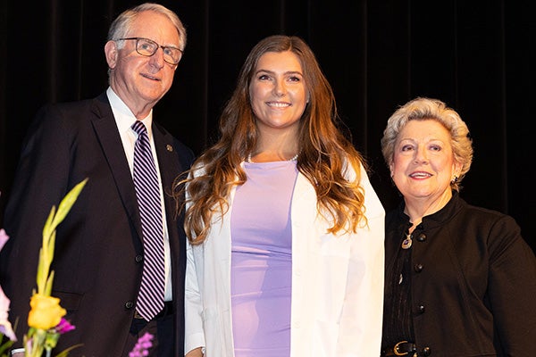 Allison Tempel, president of the dental school's Class of 2025, stands onstage with Greg Chadwick, dean, and Margaret Wilson, vice dean, after receiving her white coat.