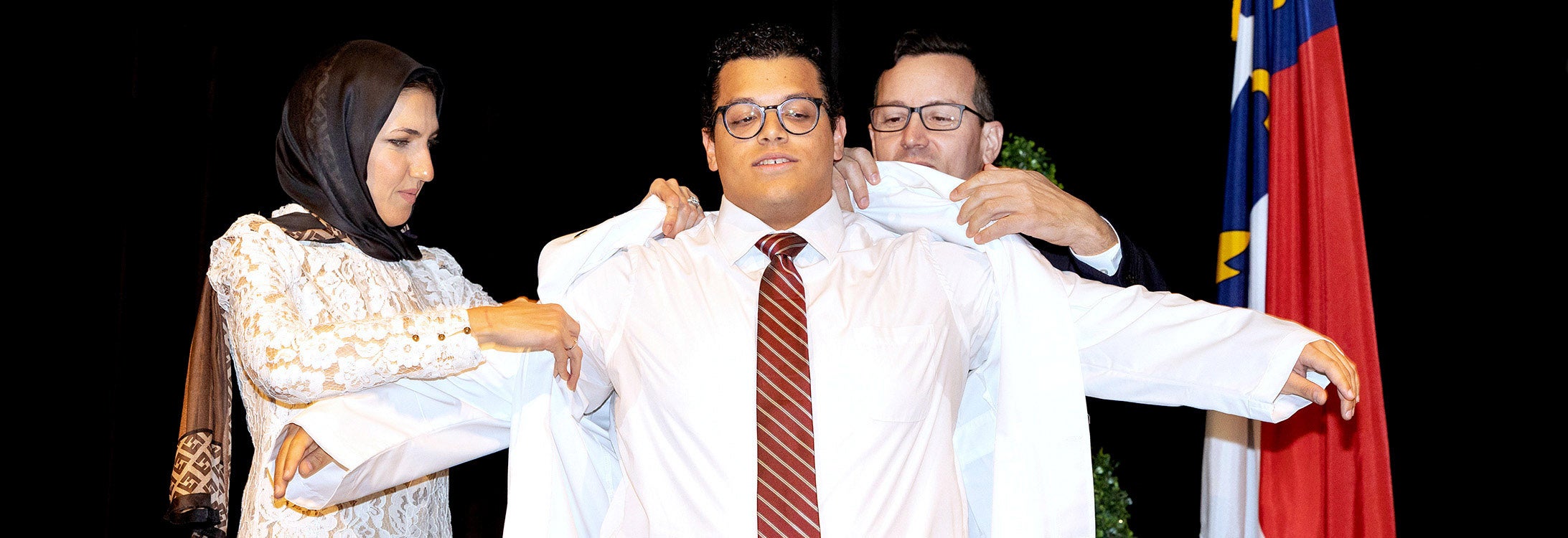 ECU School of Dental Medicine student Cesar Pelaez is helped into his white coat by faculty members Hanan Elgendy and Luis Sensi during the school’s Jan. 27 White Coat Ceremony.