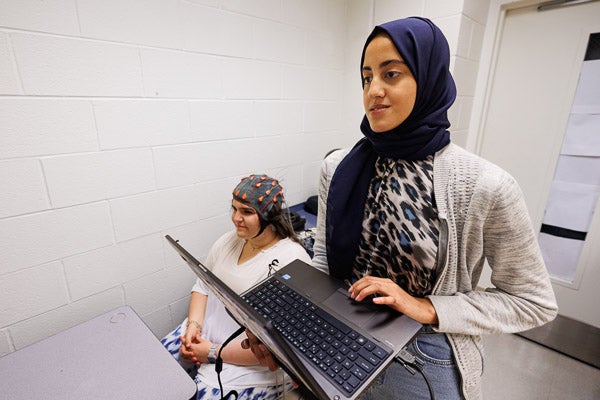 Marwa Antar, a second-year graduate student in biomedical engineering, works with a student wearing a cap that measures electrical activity in the brain. 