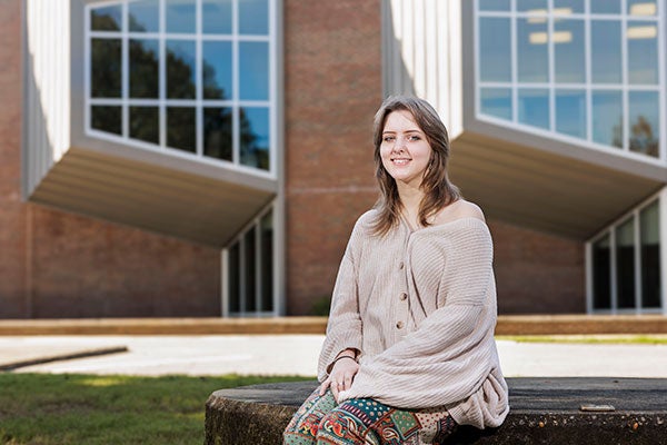 : East Carolina University senior Grace Scott smiles while sitting in front of the Jenkins Fine Arts Center.