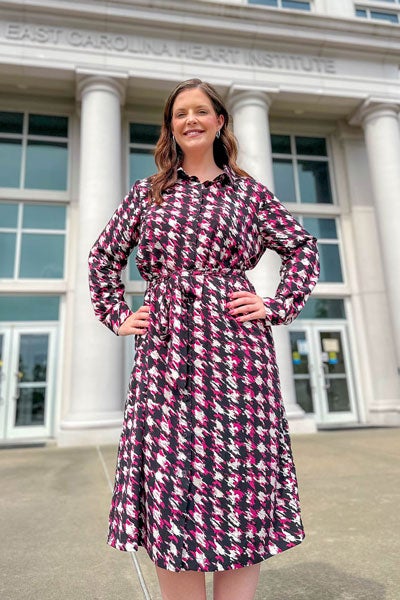 A woman with long dark hair in a patterned dress stands outside.