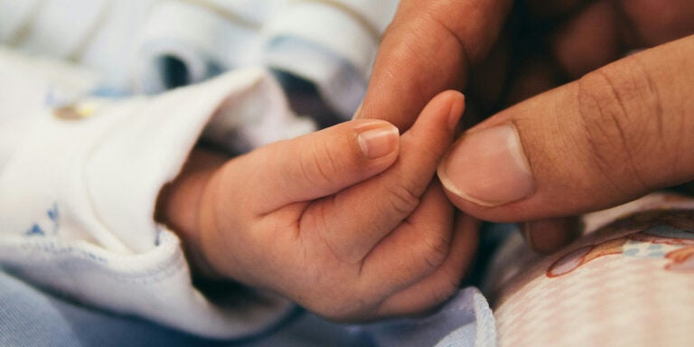 A baby’s finger is being held by an adult thumb and finger.