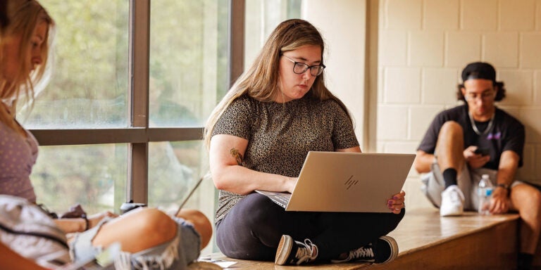 Four people sit in front of a window and look at computers held in their laps.