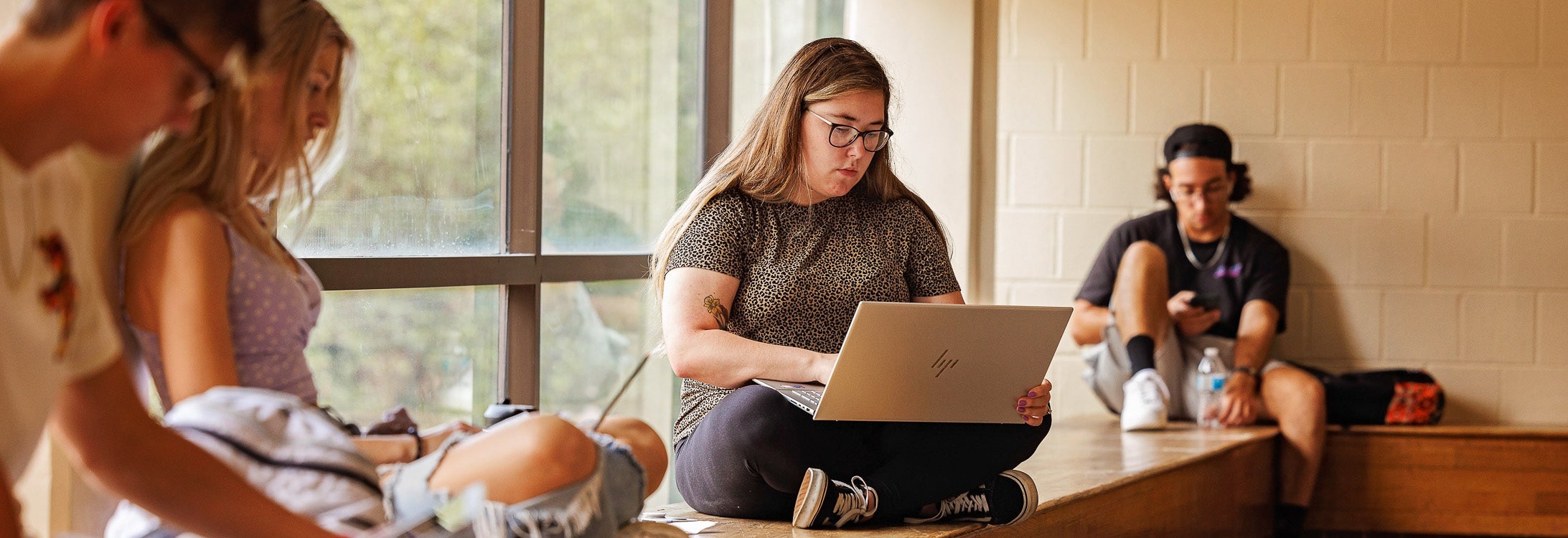 Four people sit in front of a window and look at computers held in their laps.