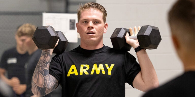 A college man lifts two weights at shoulder level.