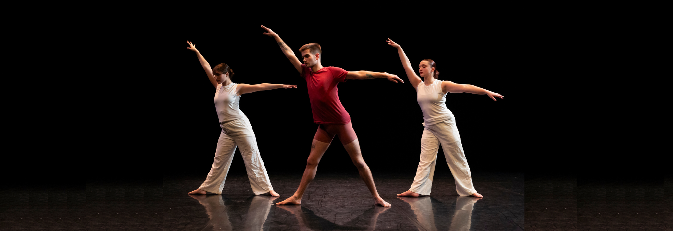 Three students stand with their arms spread while performing on stage at ECU’s McGinnis Theatre