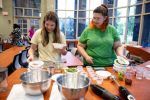Two women separate food into bowls in a well-lit indoor space.