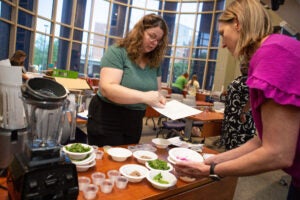 Two women put food in bowls in a well-lit indoor space.