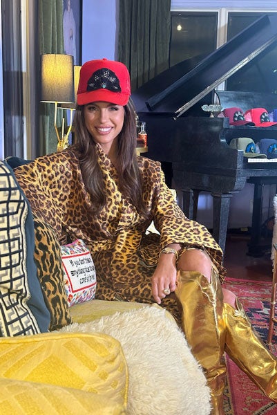 Briley King sits on a couch wearing a leopard print dress and red hat with feathers on the front.