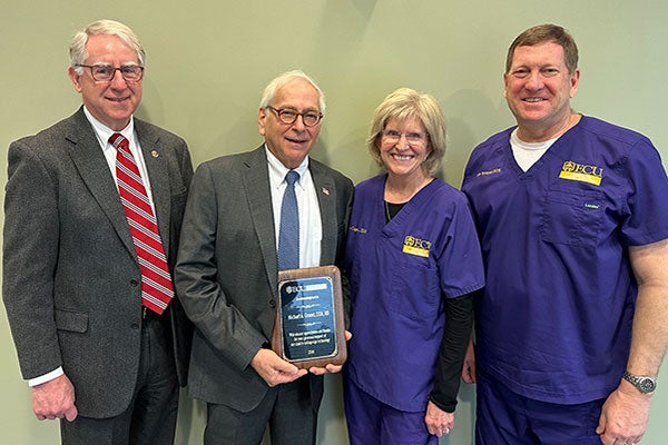 East Carolina University School of Dental Medicine Dean Greg Chadwick, Dr. Dianne Caprio and Dr. Rob Tempel Jr. honor Dr. Michael Granet, center, for his contributions to the community service learning center in Brunswick County. (Photo by Jon Jones)