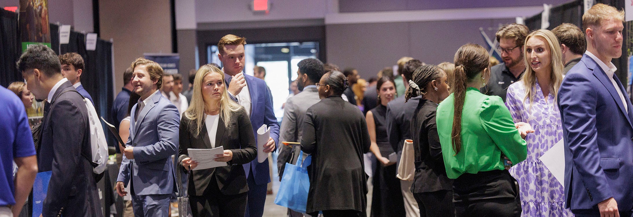 A large group of college students dressed in business attire mingle at a career fair.