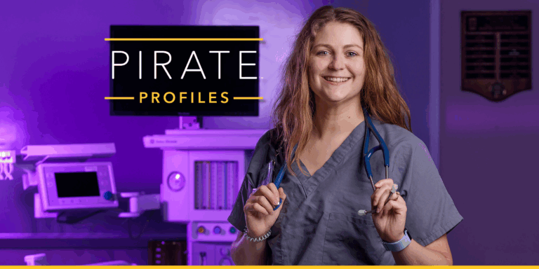 A woman in grey medical scrubs stands in a simulated operating room with purple lights.