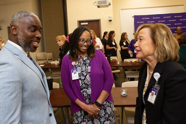 Two women and a man talk in a conference room.