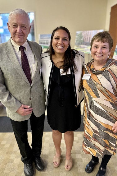 A young woman stands smiling, her arms around a couple standing on either side of her.