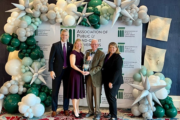 Chancellor Philip Rogers, Dr. Angela Lamson, Dr. Tom Irons and Dr. Sharon Paynter stand in front of a step-and-repeat and smile as they showcase the Magrath award.