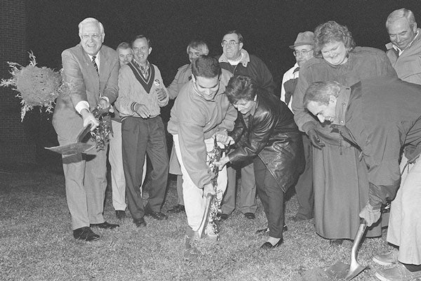 A group of people smile as they shovel dirt at a groundbreaking ceremony.