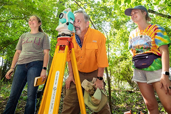 Dr. Charles Ewen, center, works with students Mackenzie Mulkey and Regina Wheeler to locate and document gravesites at an abandoned cemetery in Ayden. 