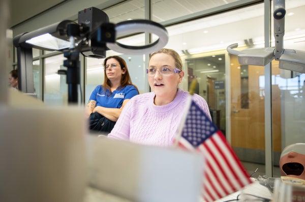 A professor in a light lilac sweater, her mouth open as she delivers remarks, sits at a lecture station that takes video of her desktop and shares with monitors at students’ stations throughout the lab.