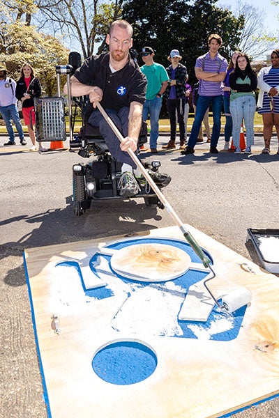 Man in wheelchair paints blue icon in parking spot.