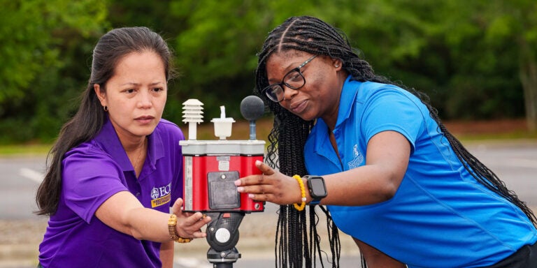 East Carolina University Health Education and Promotion professor Dr. Jo Anne Balanay and Fayetteville State University student KiHyira Jones look at a wet bulb globe temperature heat stress monitor positioned in a parking lot outside the Belk Building. They studied heat stress factors this summer.