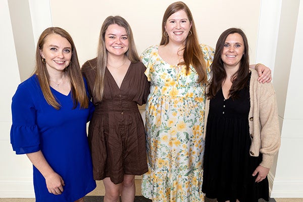 Four women in dresses and stand in a line smiling for the camera.