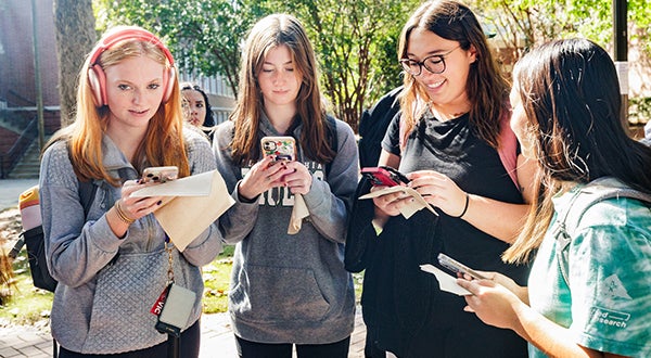 Four East Carolina University students on their cell phones out on the lawn