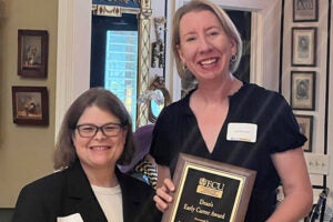 Two women stand in a room holding a plaque for the 2025 Dean’s Early Career Award.