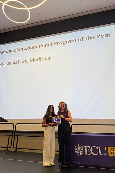 2 women standing in front of a projected screen holding an award.