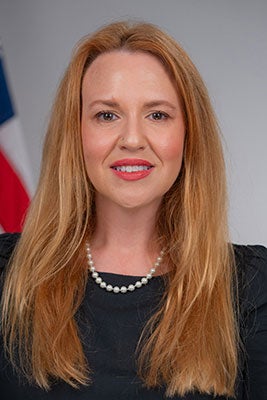 A woman with long red hair in a dark top poses for a formal photo.