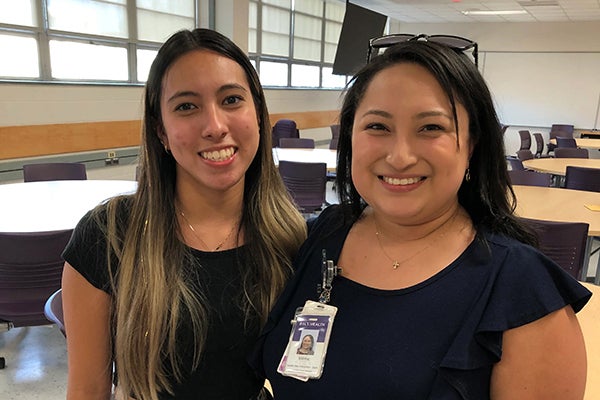 Two women with dark brown hair and black shirts stand side-by-side in a classroom on the East Carolina University campus.