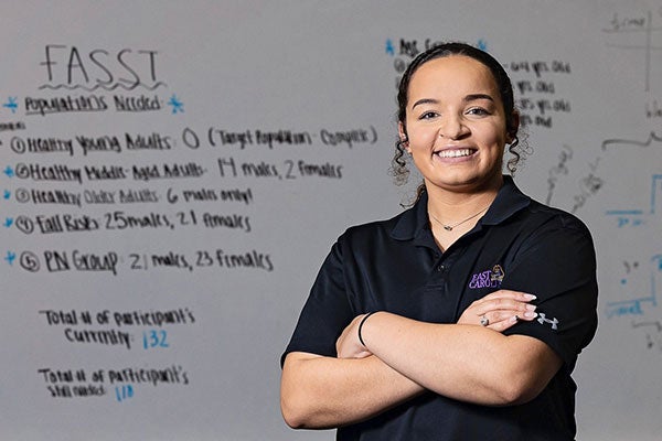 A woman with dark hair in a black shirt stands in front of a white board.