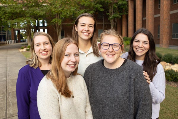 Five women stand together for a photo in an outdoor setting.