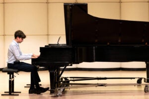 Side view of a teen playing a grand piano on a stage.