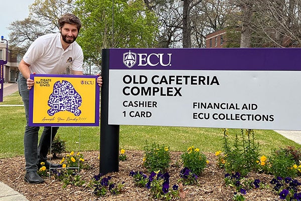 A man holds a purple and gold sign. 