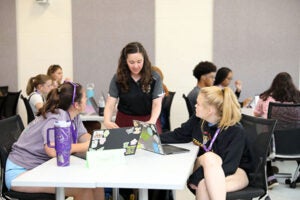 female faculty member looks at two laptops that two female students are working on