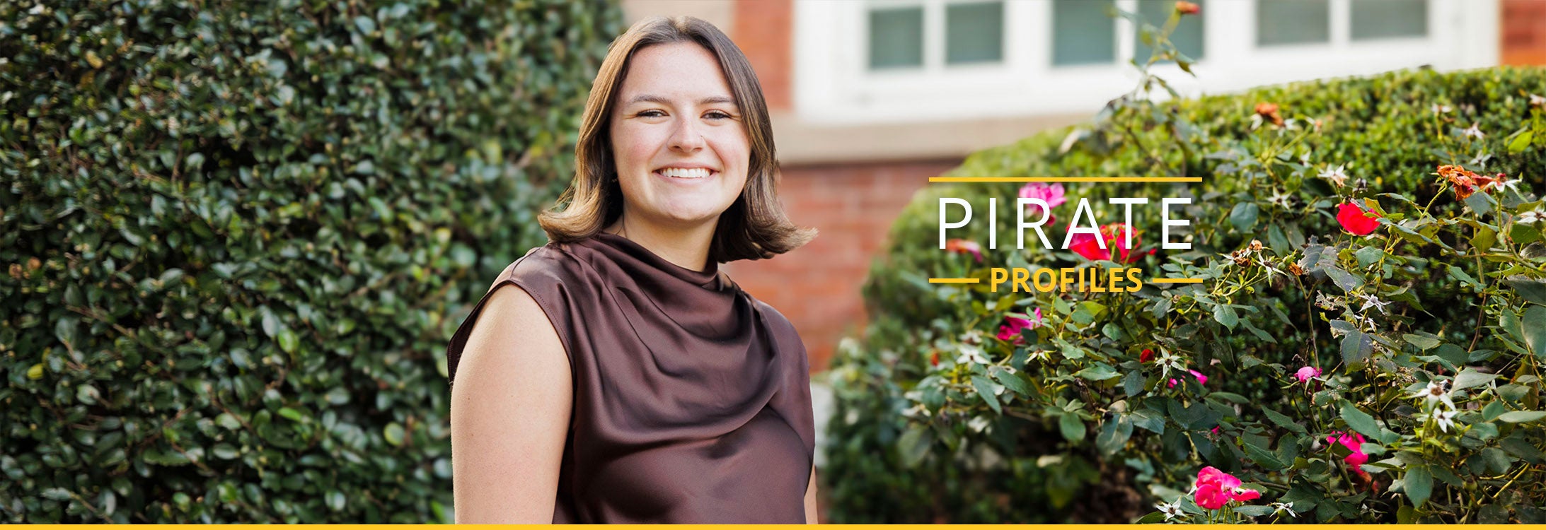 A college age woman wearing a brown top smiles as she sits on East Carolina University’s campus.