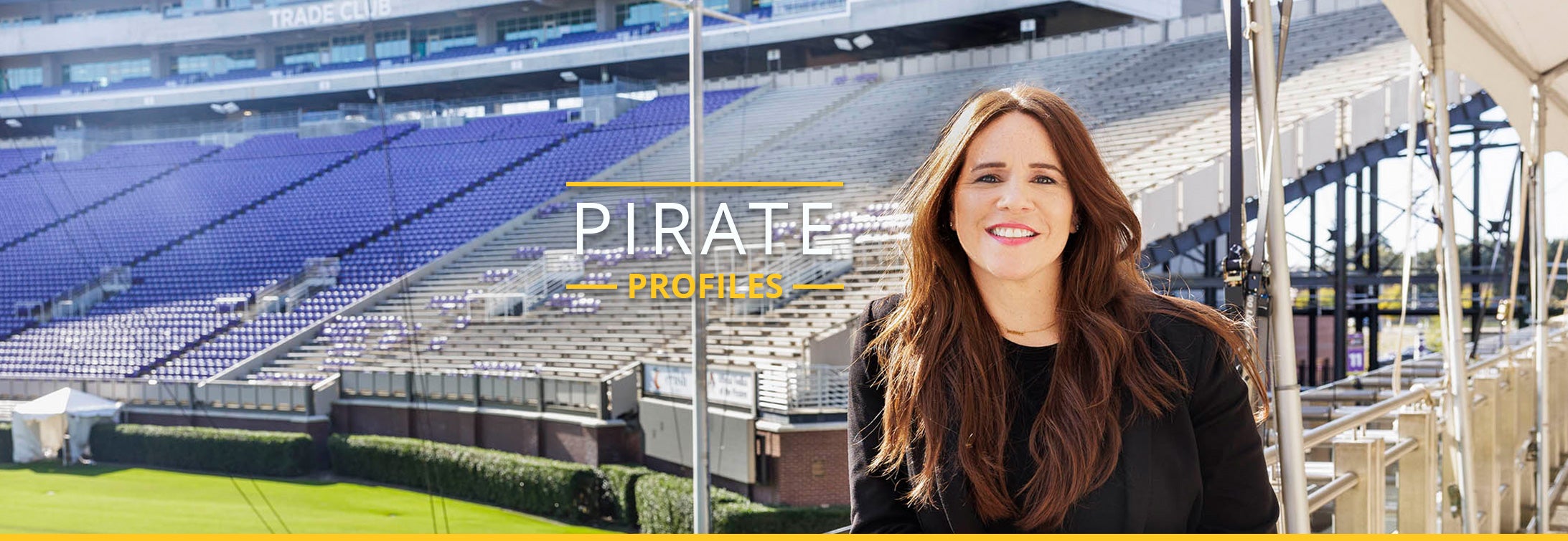 Assistant professor doctor Andrea Buenaño leans against a railing with football stadium bleachers in background.