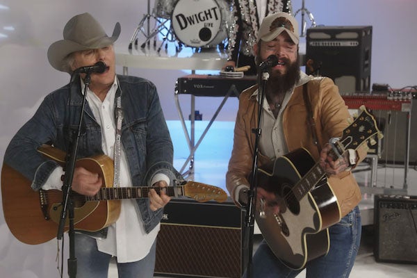 Dwight Yoakam and Post Malone stand together in a music studio holding guitars and wearing hats.