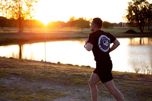 A man in a black t-shirt runs around a lake as the sun rises in the background.