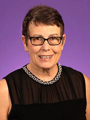 A woman with short dark hair and glasses smiles.