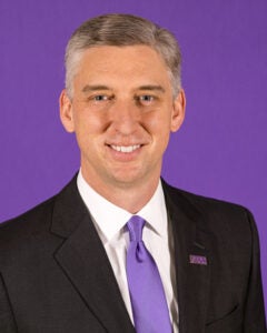 ECU Chancellor Philip Rogers smiles at the camera for his headshot as he wears a white shirt, purple tie and black suit coat.