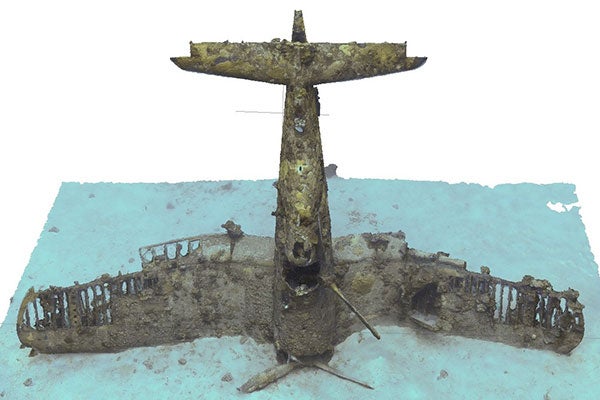 A colored, three-dimensional image of a military airplane standing upright on its nose, on the ocean floor.