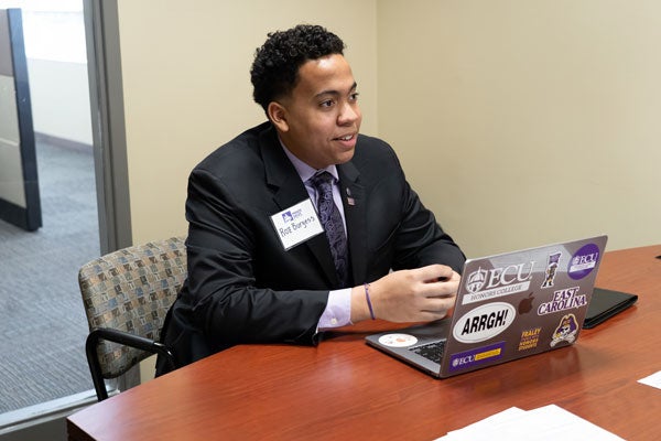 A young man wearing a costume is sitting at a table with an open laptop in front of him.