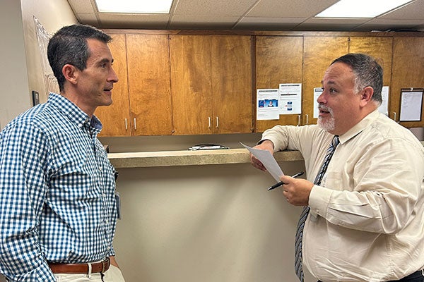  Two men stand while talking with one another in a medical clinic.