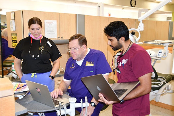 Three dental care providers consult a computer and discuss a patient case.