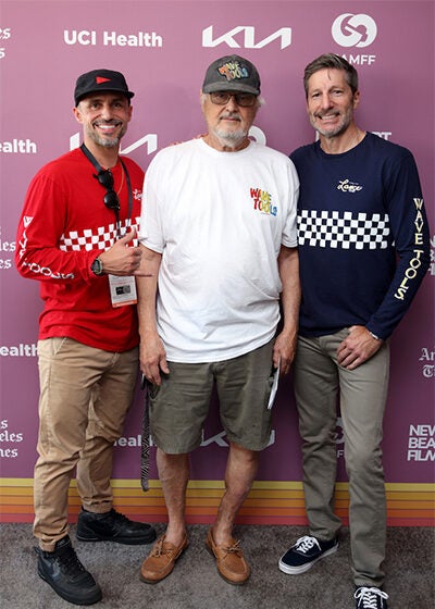 Three men in casual clothes stand side-by-side in front of a purple movie festival backdrop.