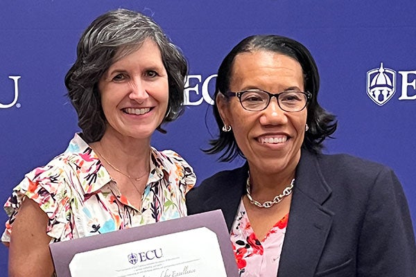 Two women stand holding awards.